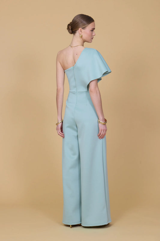 Woman wearing a light blue one-shoulder jumpsuit on a beige background