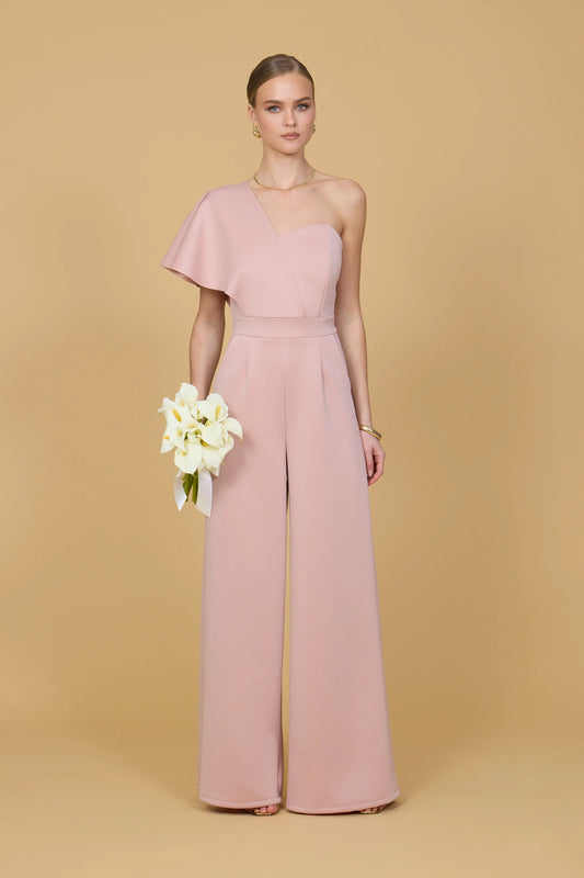 Woman wearing a pink one shoulder jumpsuit against a beige background