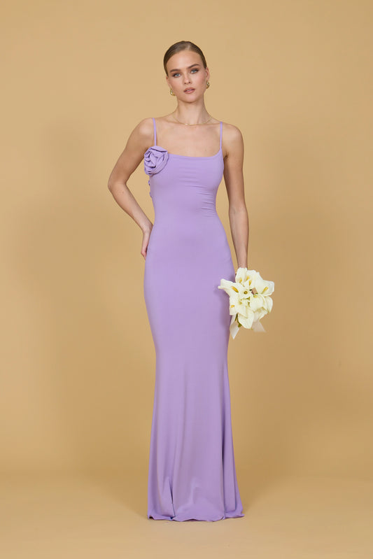 Woman in a long purple dress holding flowers against a beige background