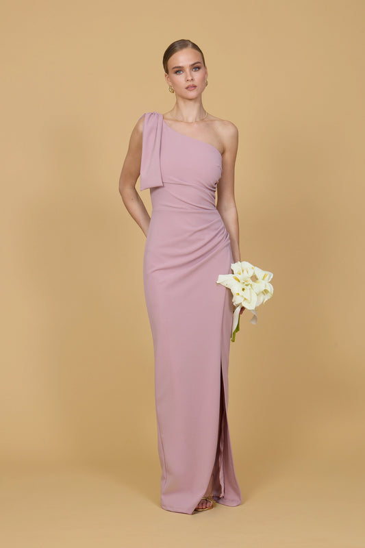 Woman wearing a one-shoulder pink gown holding flowers against a beige background