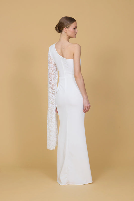 Woman wearing a white one-shoulder dress with lace sleeves against a beige background