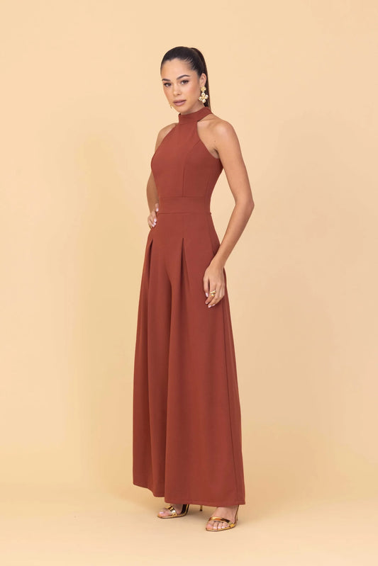 Woman wearing a rust-colored halter neck jumpsuit on a beige background