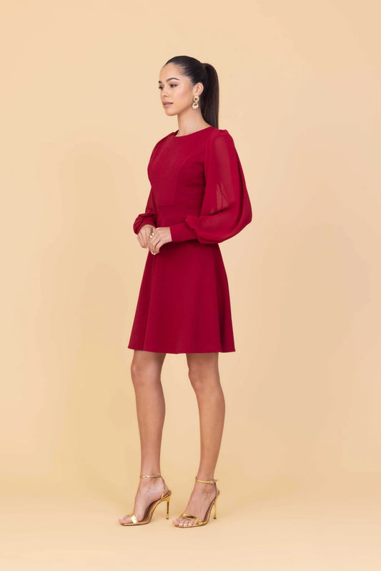 Woman wearing a red dress with sheer sleeves against a beige background