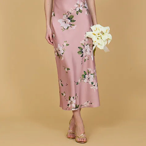 Woman wearing a pink floral dress holding white flowers against a beige background