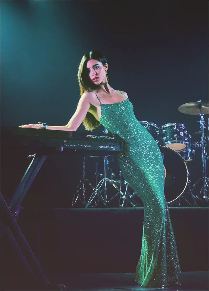 Woman in a green sparkly dress on stage with musical equipment