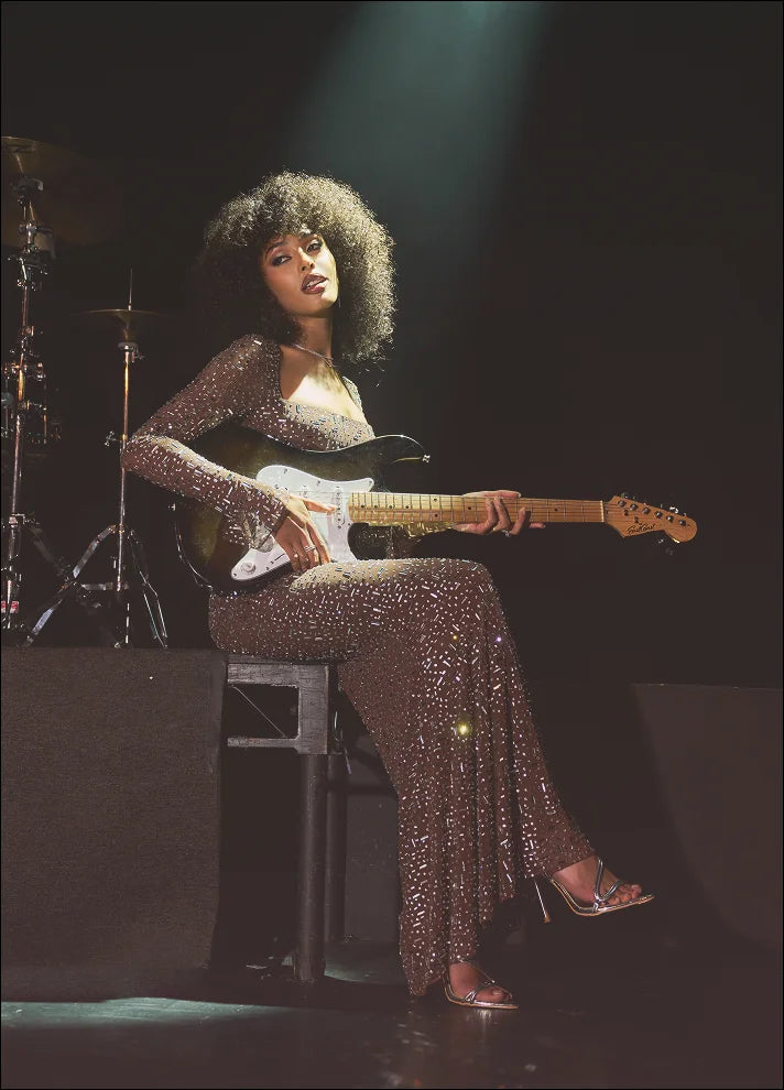 Person in a sparkly outfit playing an electric guitar on stage.