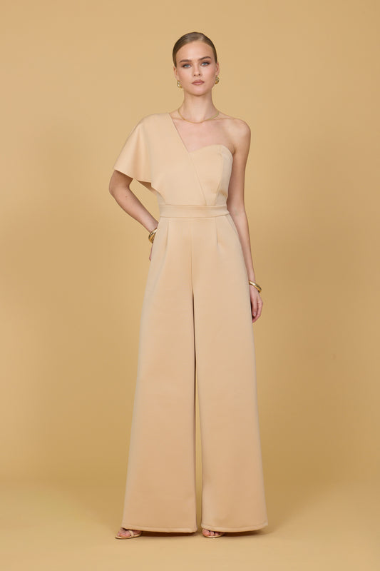 Woman wearing a light mustard one-shoulder jumpsuit on a beige background