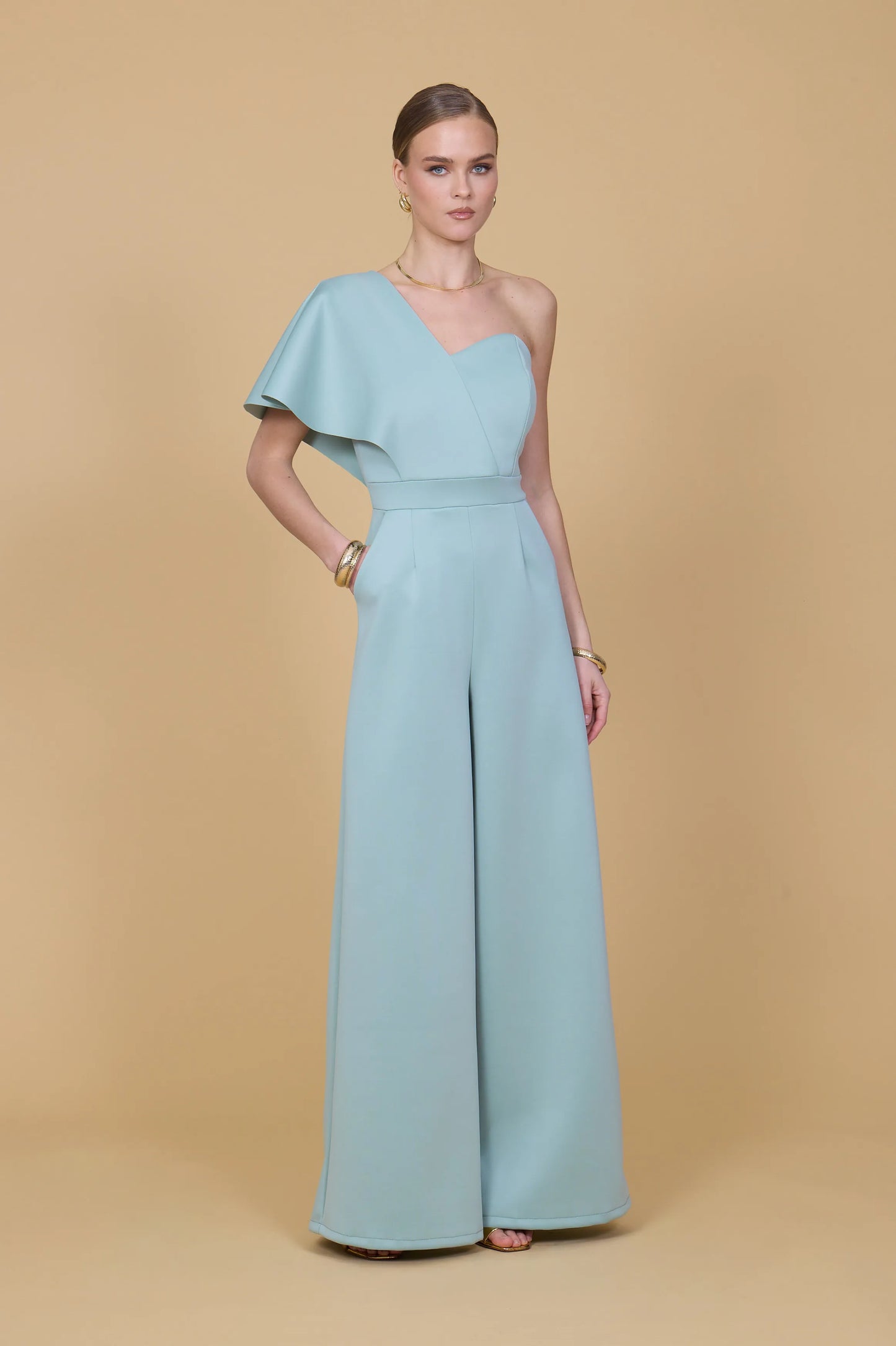 Woman wearing a light blue one-shoulder jumpsuit on a beige background