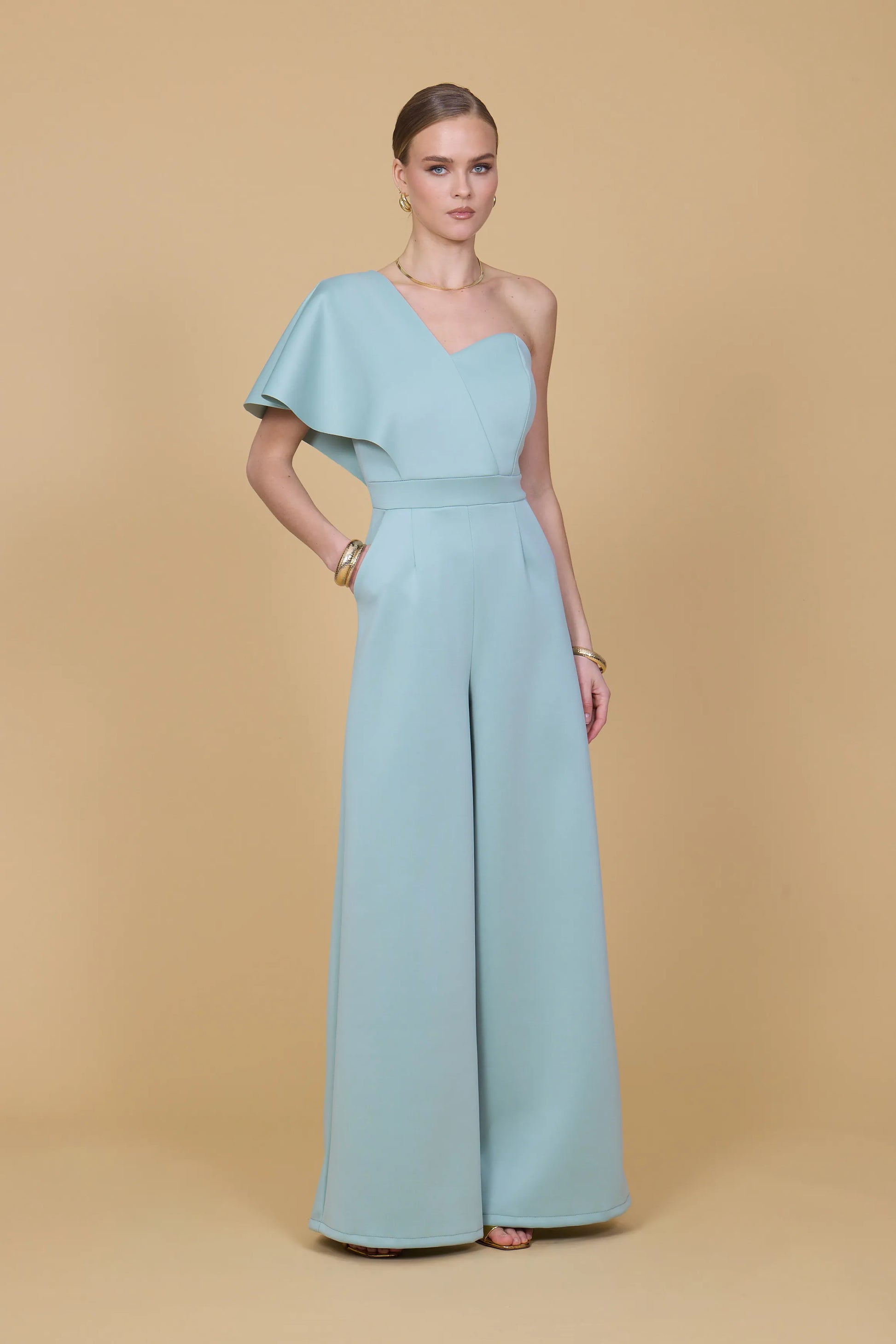 Woman wearing a light blue one-shoulder jumpsuit on a beige background