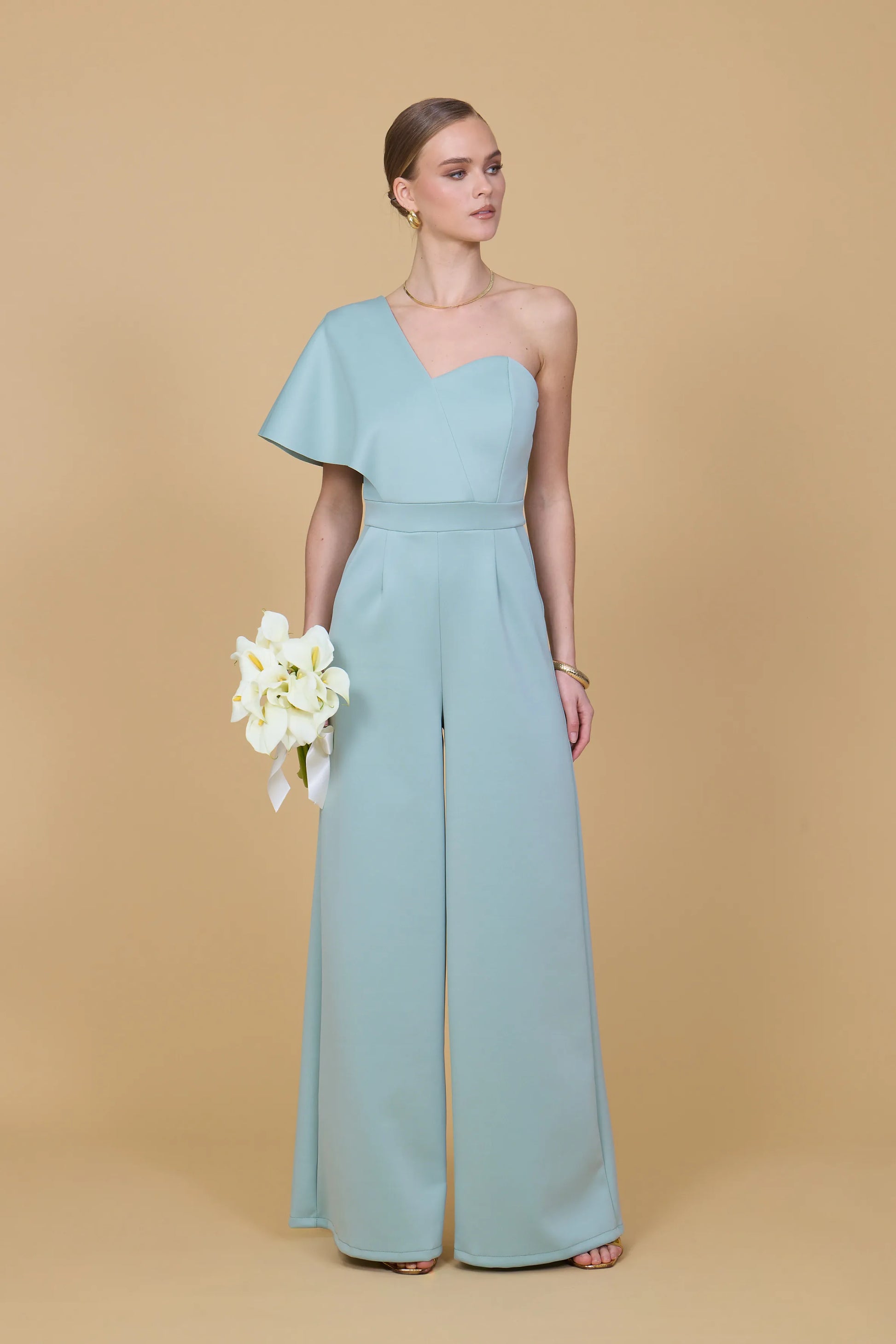Woman wearing a light blue one-shoulder jumpsuit on a beige background