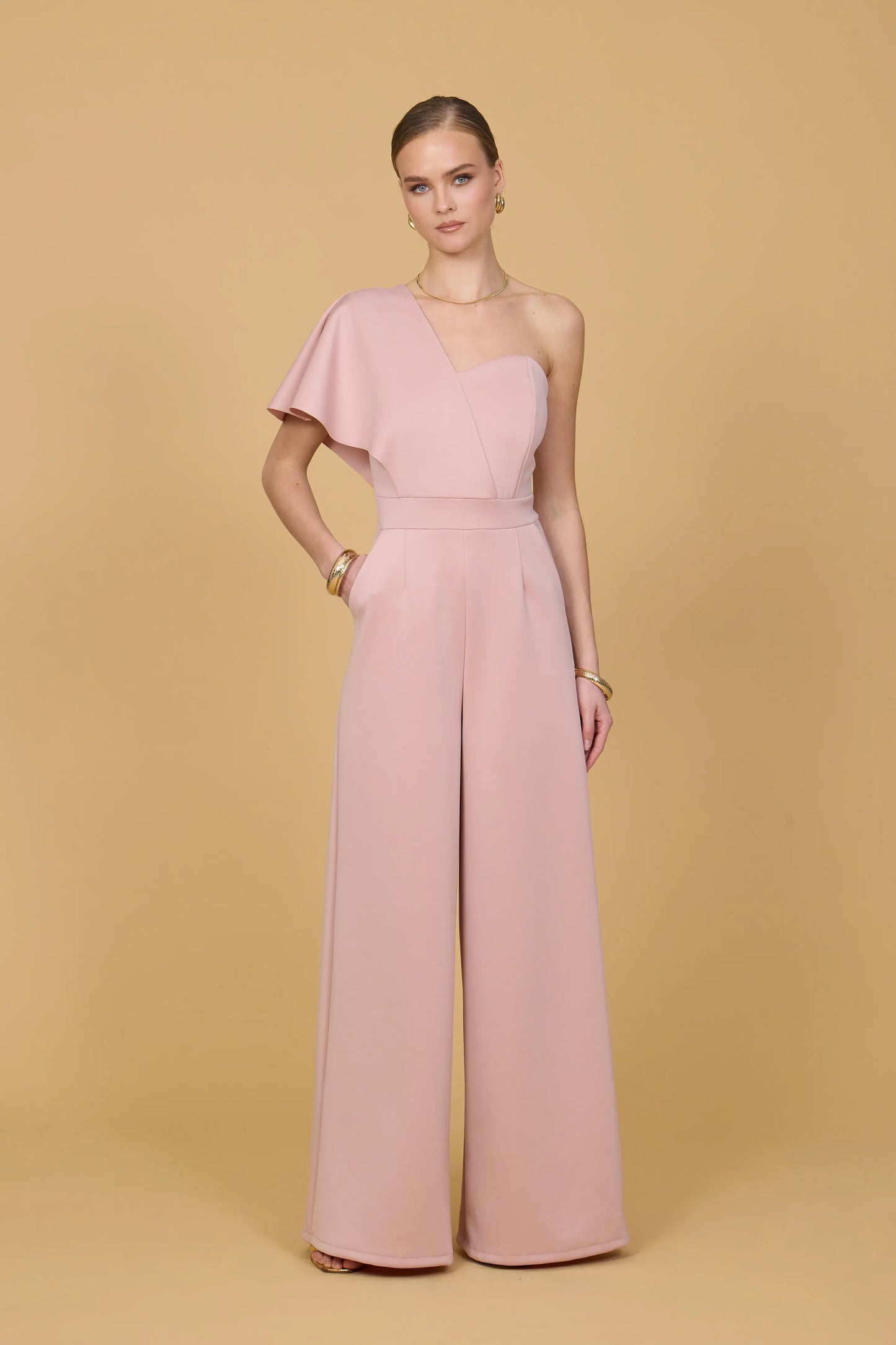 Woman wearing a pink one shoulder jumpsuit against a beige background