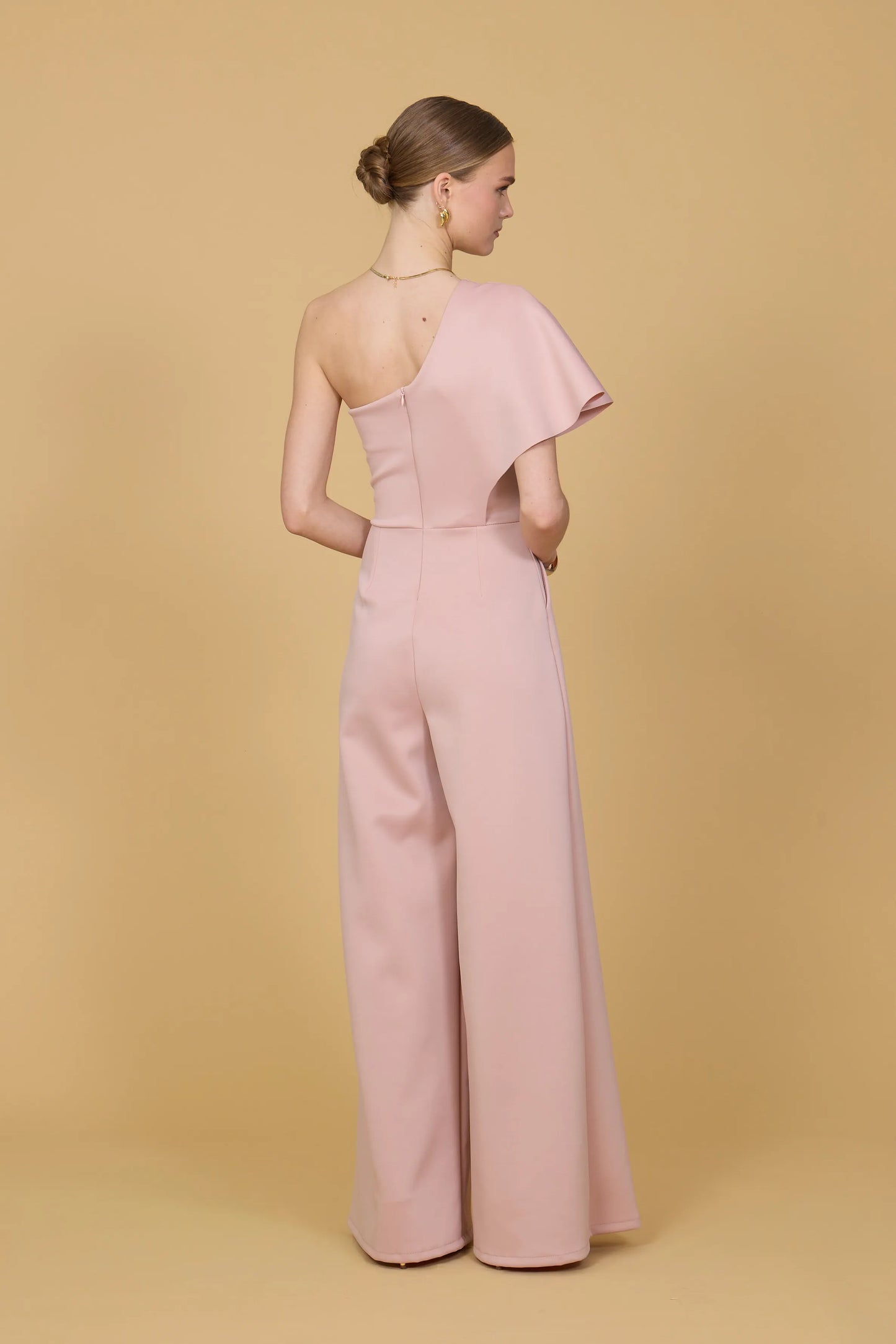 Woman wearing a pink one shoulder jumpsuit against a beige background
