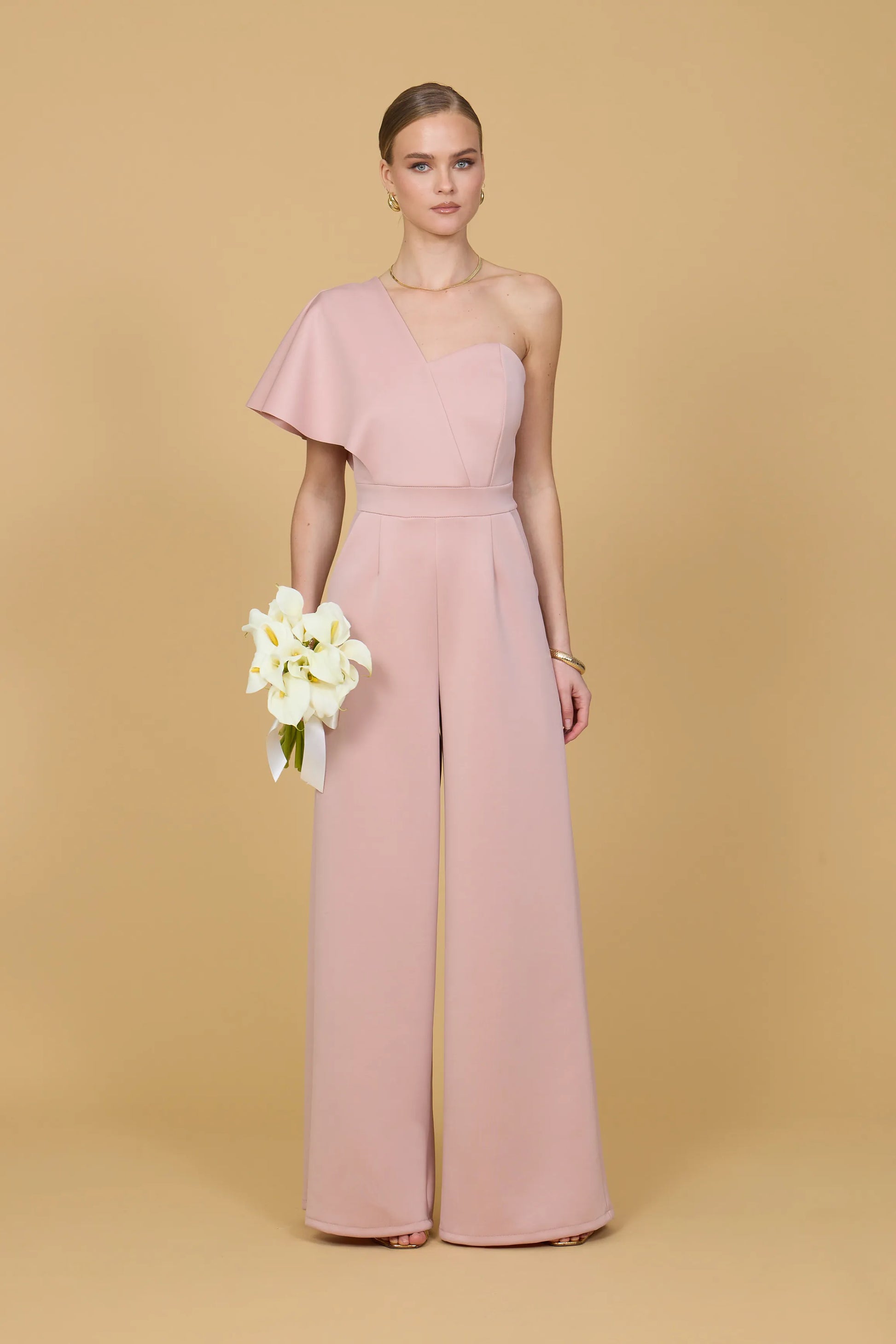 Woman wearing a pink one shoulder jumpsuit against a beige background