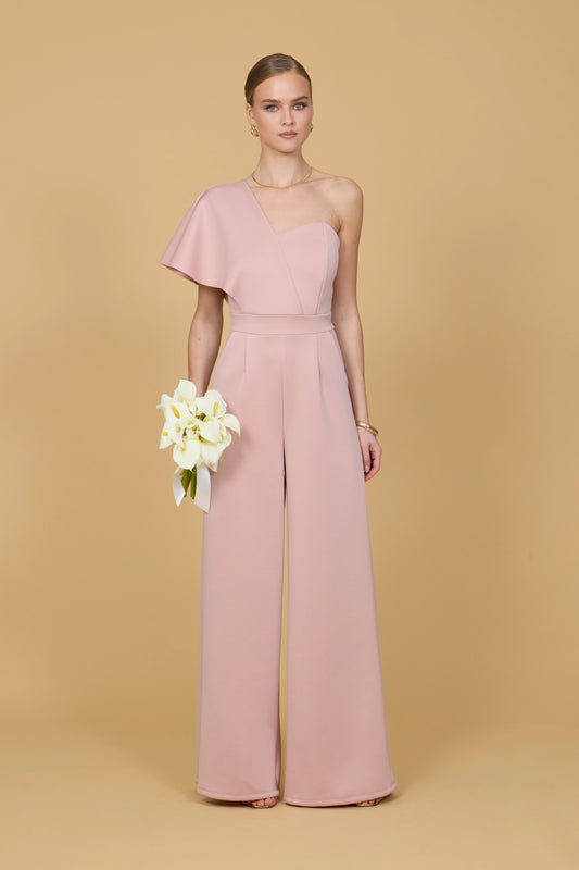 Woman wearing a pink one shoulder jumpsuit against a beige background