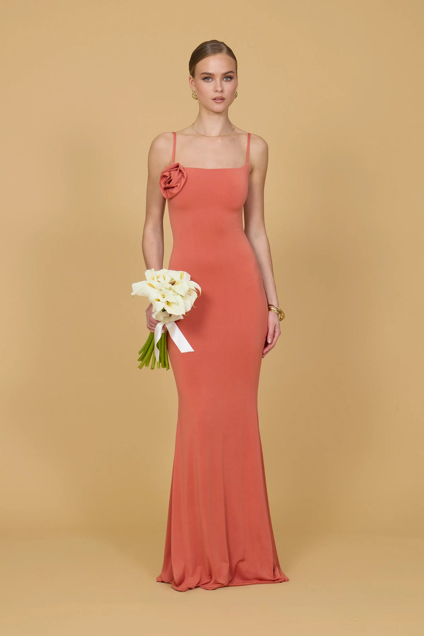 Woman in a coral dress holding flowers against a beige background