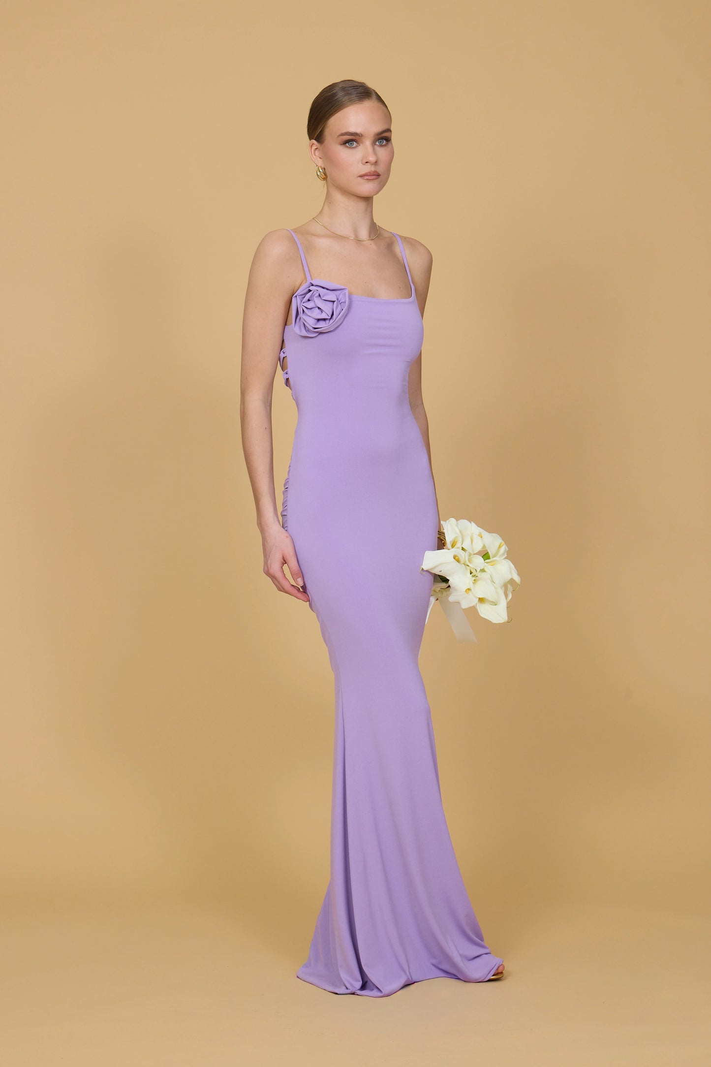 Woman in a long purple dress holding flowers against a beige background