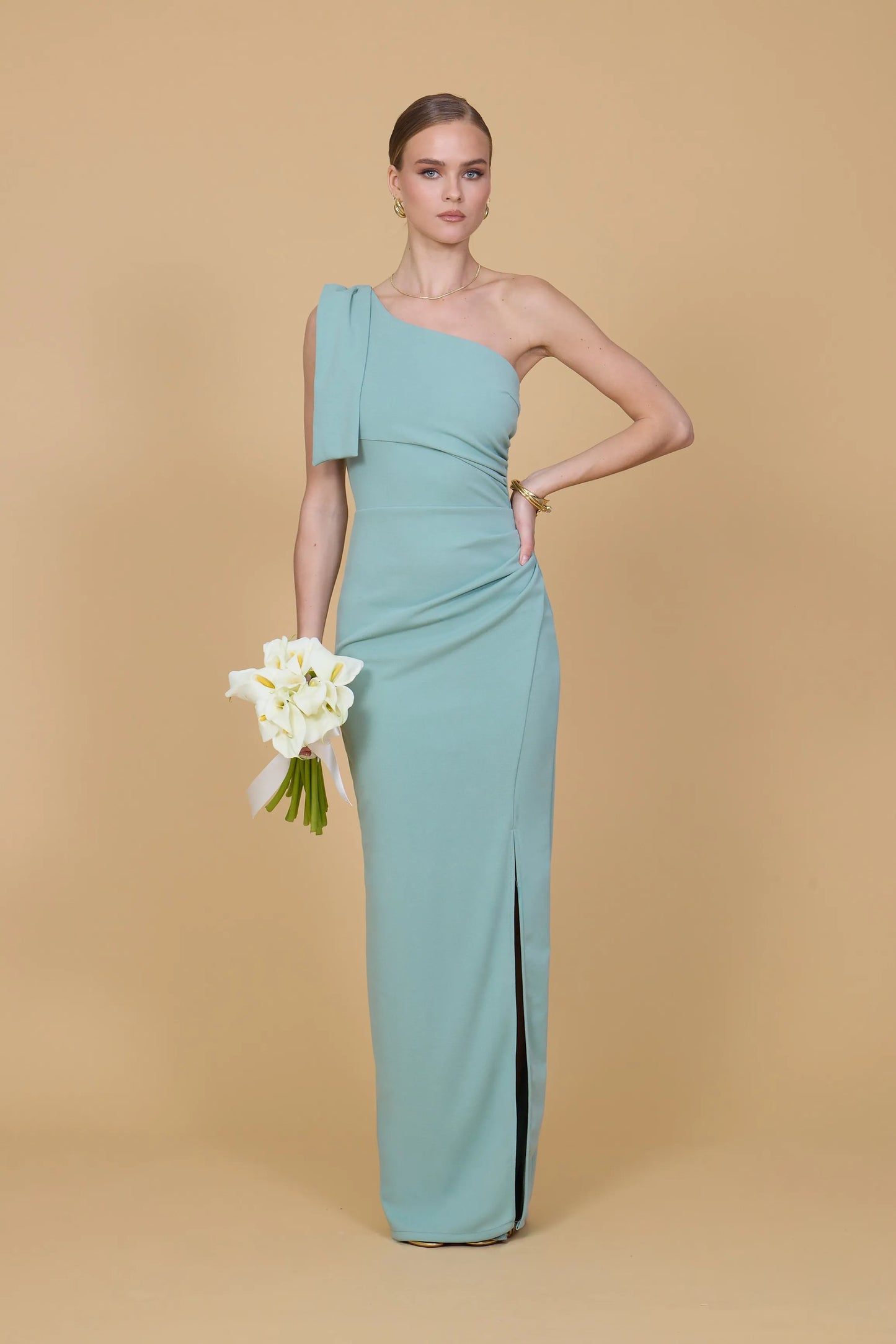 Woman in a light blue one-shoulder dress holding white flowers against a beige background
