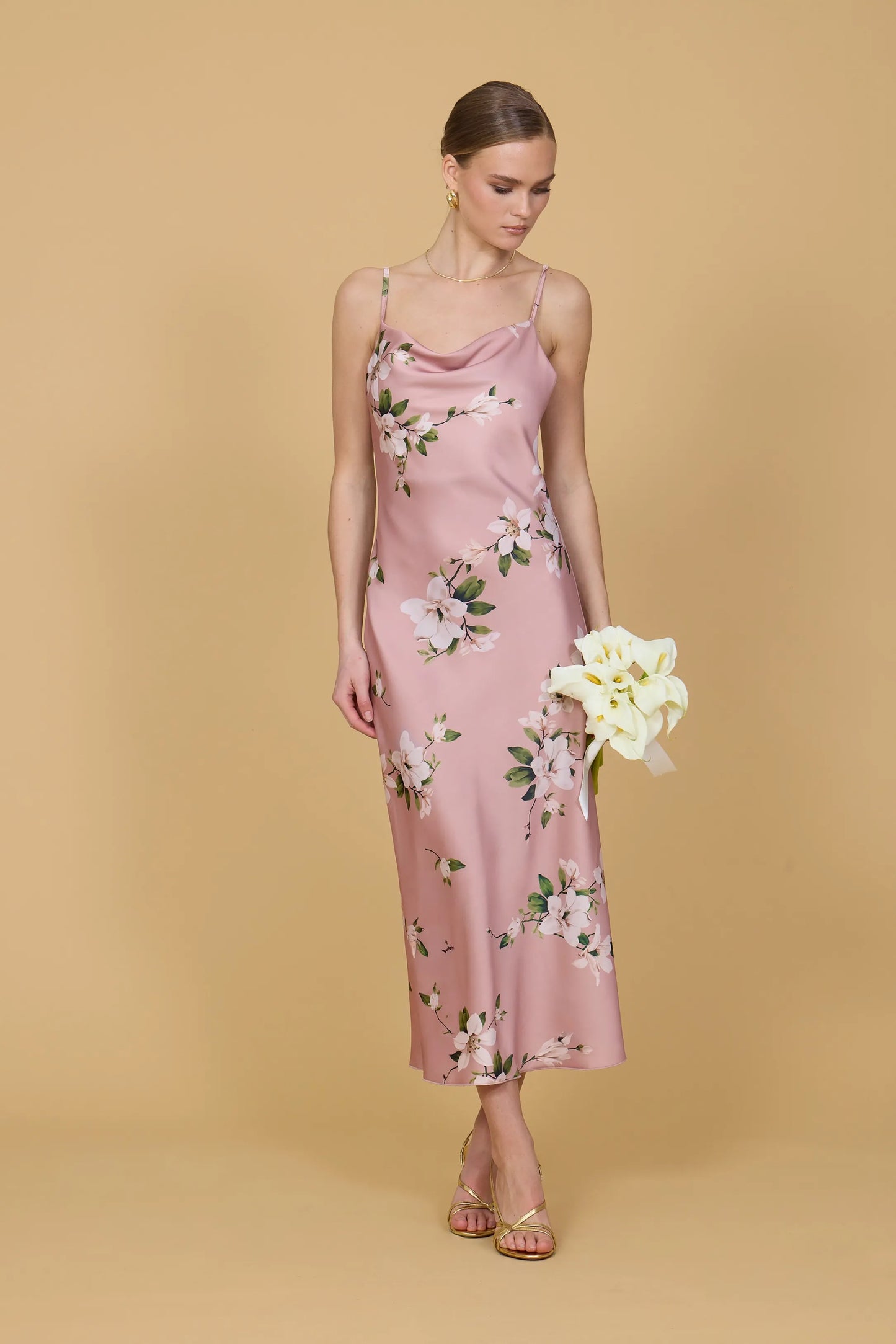 Woman wearing a pink floral dress holding white flowers against a beige background