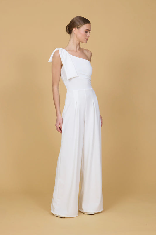 Woman wearing a white one-shoulder jumpsuit against a beige background
