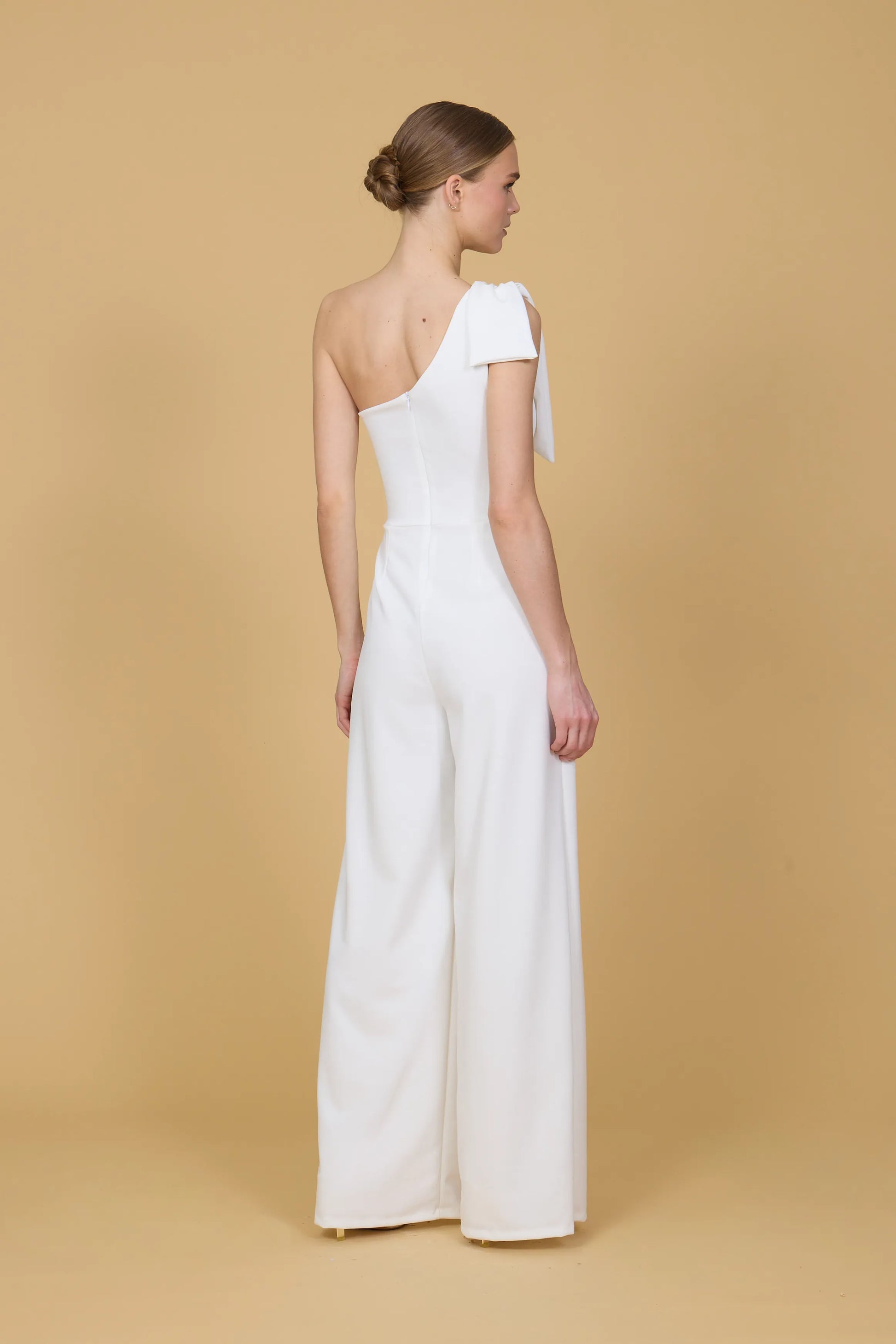 Woman wearing a white one-shoulder jumpsuit against a beige background