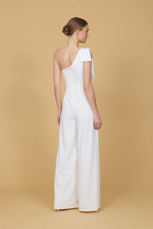 Woman wearing a white one-shoulder jumpsuit against a beige background