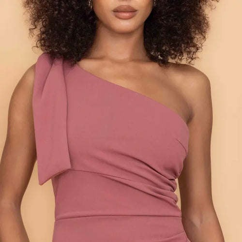 Woman wearing a one-shoulder pink dress against a beige background