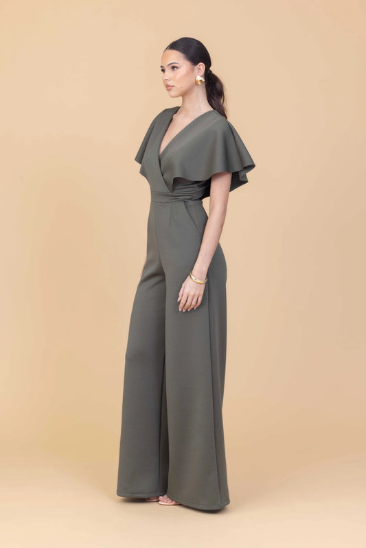 Woman wearing a green jumpsuit with ruffled sleeves on a beige background