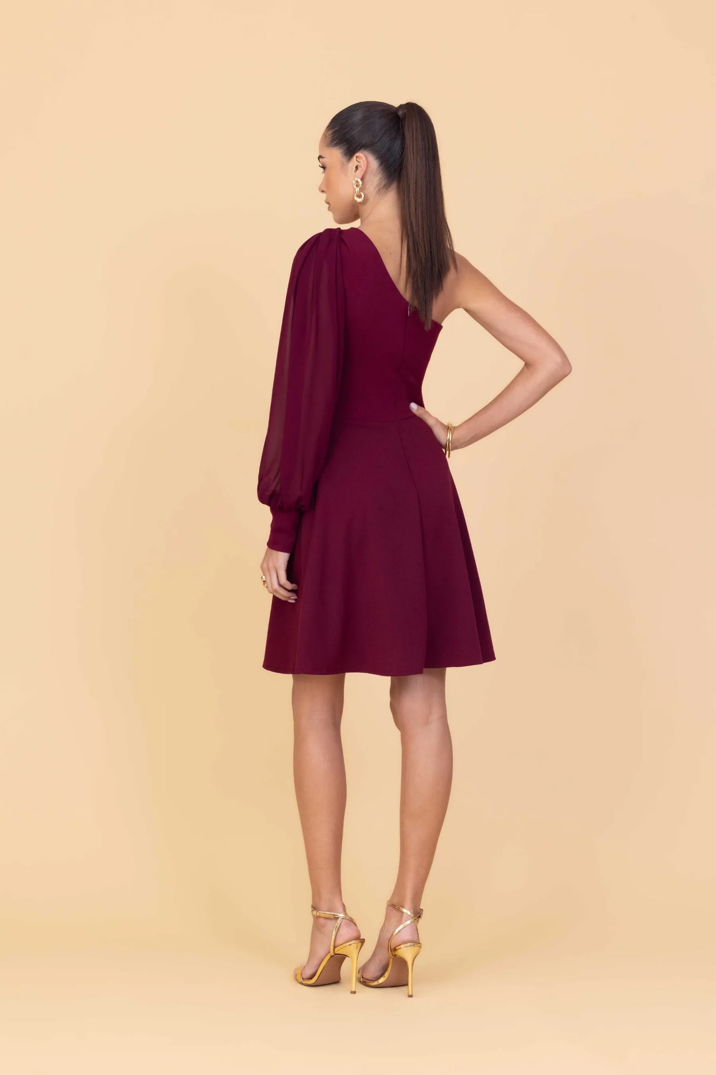 Woman wearing a burgundy one-shoulder dress on a beige background