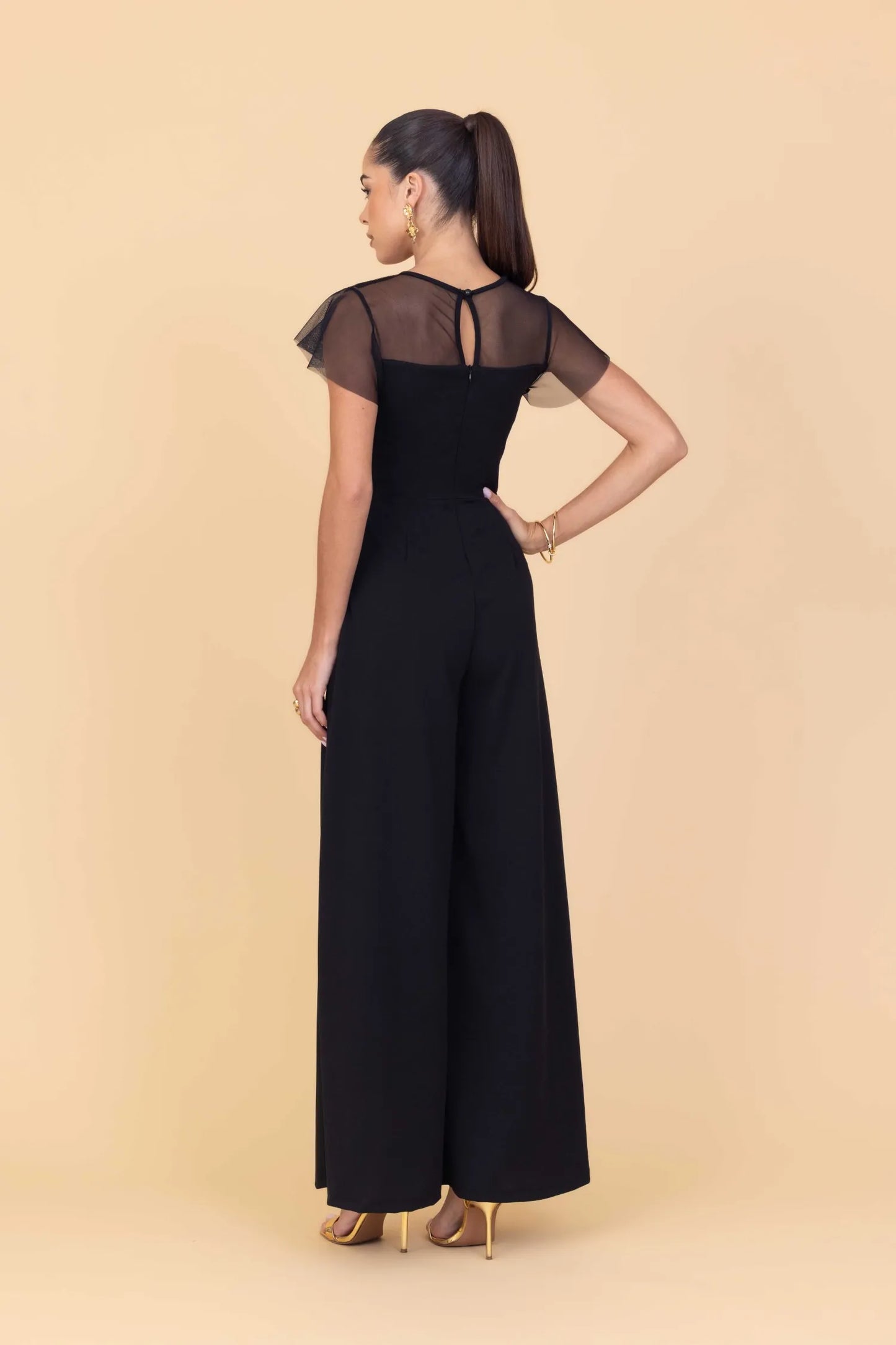 Woman wearing a black jumpsuit with sheer sleeves on a beige background