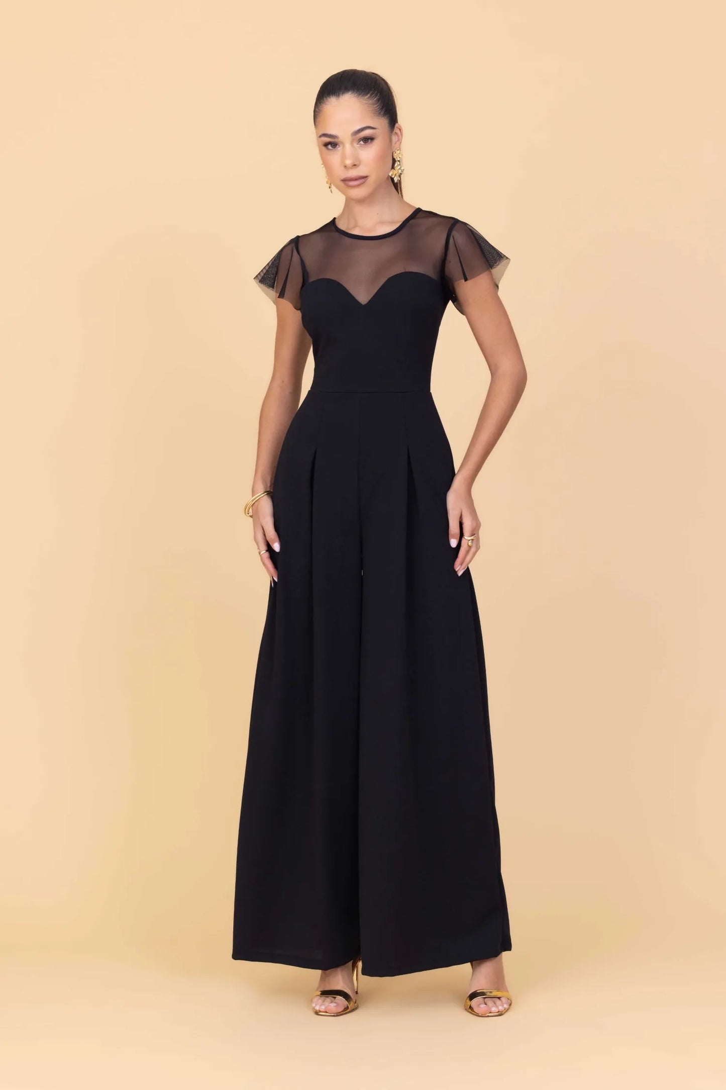 Woman wearing a black dress with sheer sleeves against a beige background