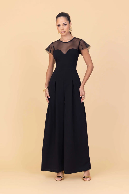 Woman wearing a black dress with sheer sleeves against a beige background