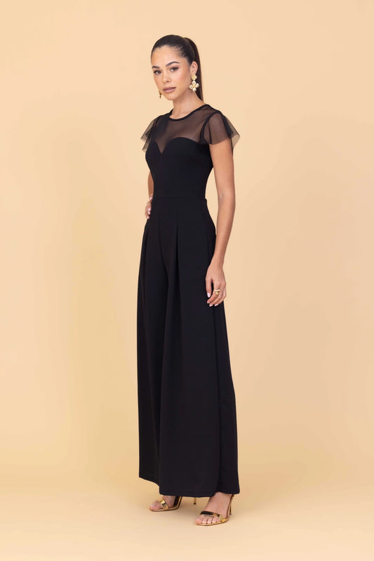 Woman wearing a black jumpsuit with sheer sleeves against a beige background