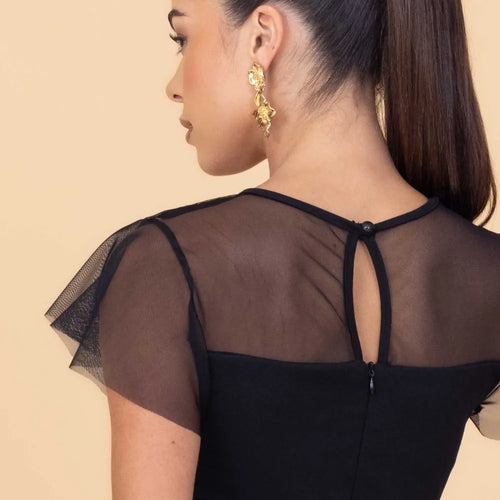 Woman wearing a black dress with sheer sleeves and back design on a beige background