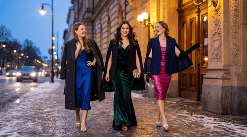 Three women in formal attire walking on a city street at night.